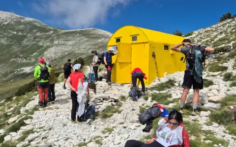 Gruppo di escursionisti vicino a un giallo blockhaus Majella, su un sentiero roccioso con montagne verdi sullo sfondo.