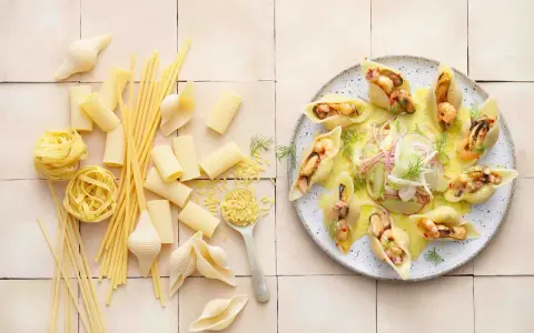 Gefüllte Conchiglioni mit Meeresfrüchten, ein köstliches italienisches Rezept. Daneben verschiedene italienische Pasta-Sorten.