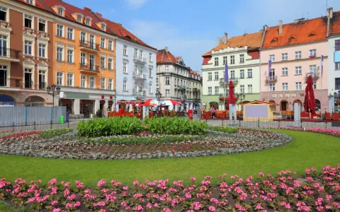 Kolorowy rynek w najstarszym mieście w Polsce, z kwitnącymi rabatami kwiatowymi i kamienicami.