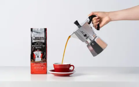 Popularna kawa Bialetti Moka wylewa się z kawiarki do czerwonej filiżanki.