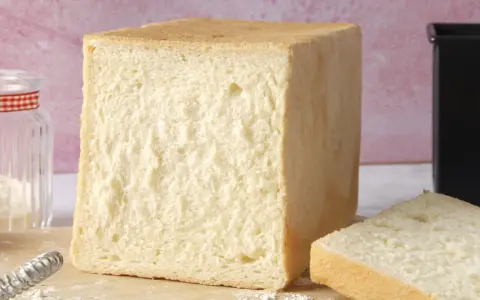 Un pain de mie moelleux, parfait pour une recette facile. Un pot de farine et un moule à pain sont à proximité.