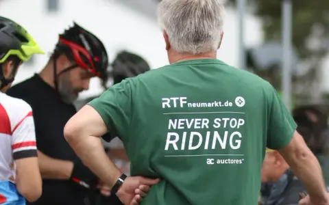 Männer in Radlerkleidung, einer trägt ein grünes T-Shirt mit der Aufschrift "RTFneumarkt.de NEVER STOP RIDING".