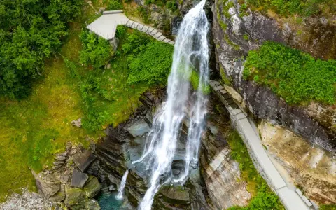Majestätischer norwegischer Wasserfall stürzt in ein türkisfarbenes Becken. Wege führen Besucher nah heran.
