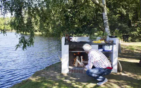 Man tänder en brasa i en nybyggd grill av tegelstenar vid en sjö.