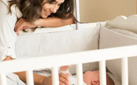 Madre sonríe a su bebé en la cuna. Un momento tierno para empezar a enseñar a un bebé a enlazar ciclos de sueño.