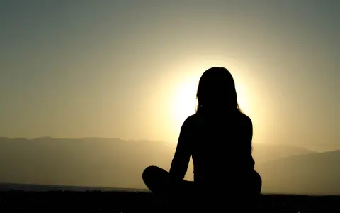 Silhuett av en person som mediterar vid solnedgången. Kanske är det en av nackdelar med meditation att man blir så fokuserad att man missar allt annat.