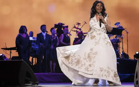 Aretha Franklin w białej sukni z haftem, śpiewa na scenie z chórem. Jej dzieci z pewnością byłyby dumne.