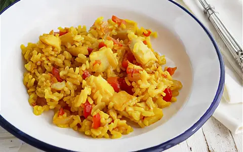 Arroz amarillo con trozos de bacalao y pimientos rojos en un plato blanco.