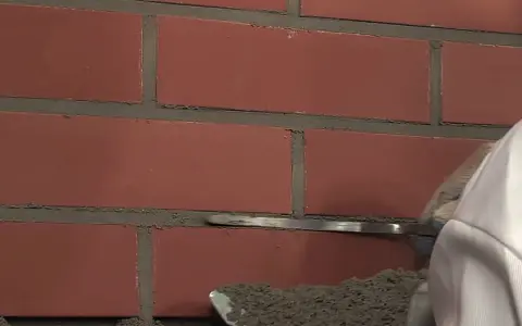Prace przy ścianie z cegły klinkierowej. Narzędzie do fugowania zbiera zaprawę, przygotowując do czyszczenia klinkieru.