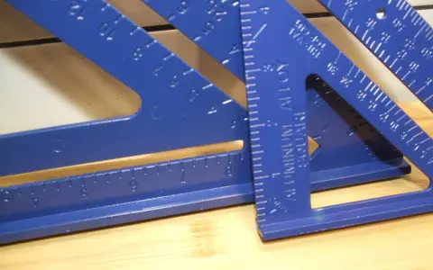 Niebieskie kątowniki stolarskie, jeden z nich z napisem "ALUMINUM SQUARE", leżą na drewnianym blacie.