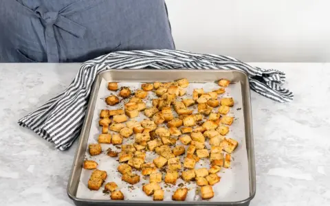 Una teglia piena di crostini di pane dorati e croccanti, conditi con erbe aromatiche. Perfetti per insalate o zuppe.