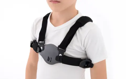Dziecko w białej koszulce nosi czarny stabilizator klatki piersiowej, który pomaga korygować wypukłą klatkę piersiową.