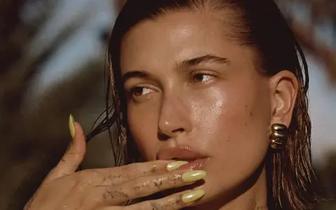 Mujer con brillos en la cara, uñas amarillas y tatuajes en la mano.