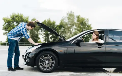 Un hombre revisa el motor de un coche negro mientras una mujer espera en el asiento del conductor. Intento arrancar el coche y no hace nada.
