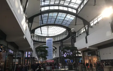 Helles, modernes Einkaufszentrum mit Glasdach. Menschen schlendern durch das Oberhausen Centro, vorbei an Geschäften wie Lacoste.