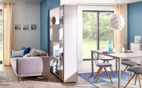 Aménagement salle à manger moderne avec canapé confortable et table design. Une étagère sépare les espaces.