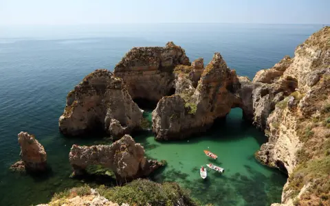 Felsformationen mit Bögen im türkisfarbenen Meer, Boote fahren vorbei. Perfektes Wetter Portugal September für einen Ausflug.