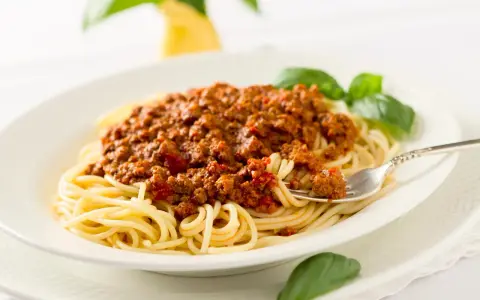 Ein Teller Spaghetti mit einer reichhaltigen, traditionell zubereiteten Bolognese-Sauce, garniert mit frischem Basilikum.