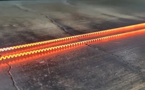 Dos espirales incandescentes, demostrando el efecto Joule en una caldera, brillan con un naranja intenso sobre una superficie oscura y agrietada.