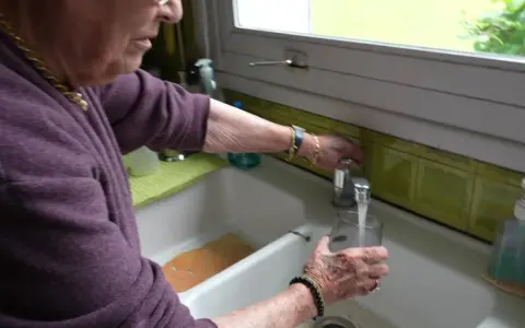Une femme remplit un verre d'eau du robinet. L'eau de Beauvais coule fraîchement.