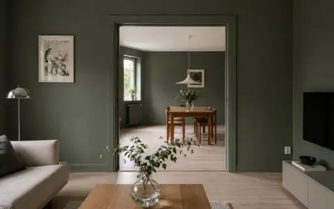 Vardagsrum med soffa och ett öppet dörrhål till matsal med träbord. **Inmålade lister** ger en enhetlig känsla.