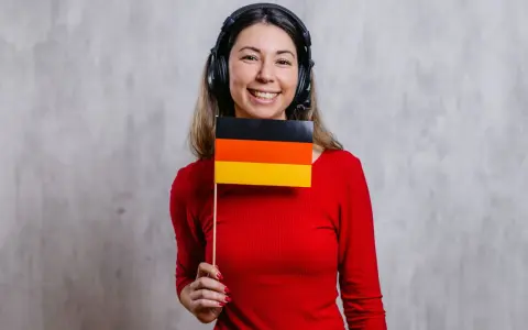 Uśmiechnięta kobieta w słuchawkach trzyma flagę Niemiec. Czy to jej nowy nauczyciel języka niemieckiego?