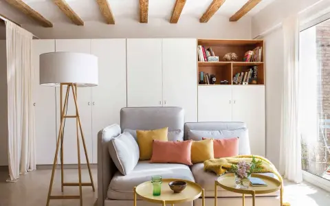 Sofá gris con cojines coloridos, mesa auxiliar amarilla y lámpara de pie. Ideas para decorar piso alquiler low cost con estilo y calidez.