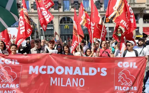 Manifestanti con bandiere rosse chiedono un miglior stipendio McDonald's a Milano.