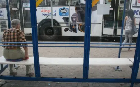 Mężczyzna czeka na przystanku na autobus 102. Rozkład jazdy jest niewidoczny, ale widać autobus z reklamą Allegro.