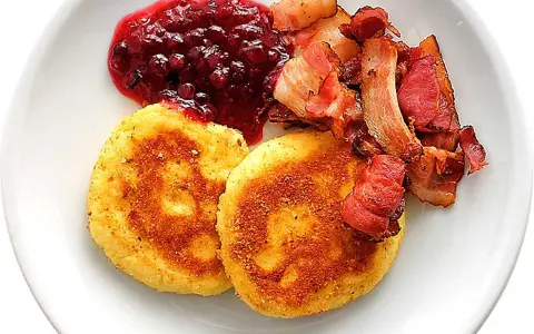Två gyllene potatisbullar med lingonsylt och knaperstekt bacon. Ett klassiskt recept på potatisbullar som passar perfekt till frukost eller middag.