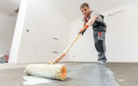 Man målar garagegolv med en roller.