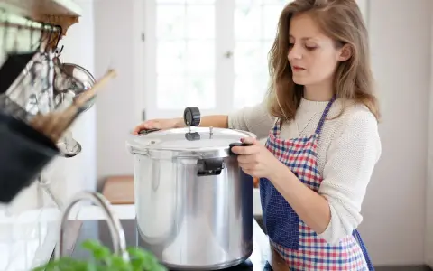 Junge Frau mit Schürze bereitet gebratenes Fleisch zum Einkochen in einem Schnellkochtopf vor.