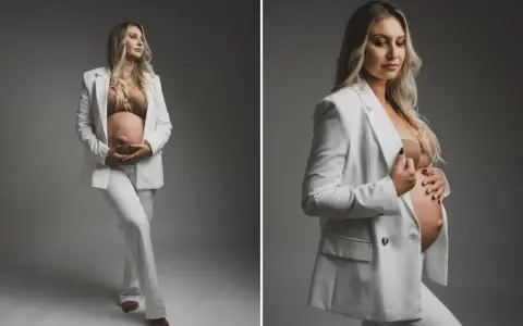 Elegancka kobieta w białym garniturze podczas sesji ciążowej, czule trzymająca się za brzuch.