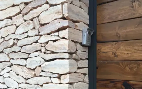 Mampostería concertada de piedra natural con un intercomunicador plateado en la esquina, junto a una pared de madera oscura.