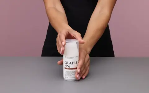 Hände halten eine Flasche Olaplex Nr. 6 Bond Smoother, ein Leave-in Styling Treatment für Feuchtigkeit und Stärke.