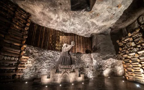 Kopalnia soli Wieliczka ciekawostki: rzeźba górnika Mikołaja Kopernika w solnej komorze, otoczona drewnianymi belkami i solnymi ścianami.