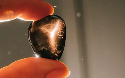 Dedos sostienen una piedra oscura con destellos dorados. ¿Qué pasa si se rompe una piedra energética? Quizás solo se dispersa su luz.
