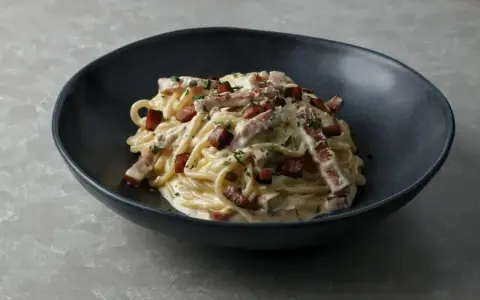 Pyszne spaghetti carbonara w ciemnej misce, idealne do nauki, jak zrobić carbonare.