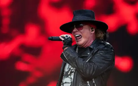 Axl Rose sjunger med en röd bakgrund. Trots rykten om axl rose sjukdom, levererar han en energisk show.