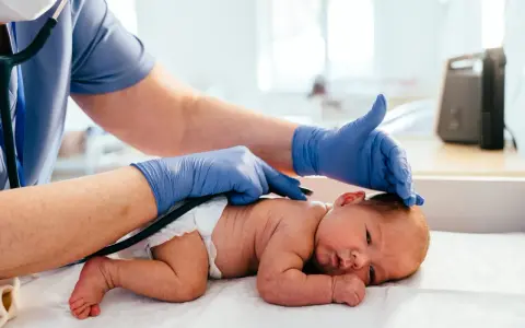 Medico controlla la schiena di un neonato, notando una piccola fossetta sacrale.