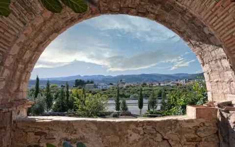 Vista de un pueblo desde un arco de ladrillo. Un paisaje con montañas y vegetación, ideal para ver en altura.