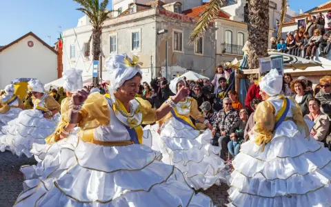 Menschen in Portugal feiern ausgelassen. Frauen in prachtvollen weißen und goldenen Kleidern mit Rüschen tanzen fröhlich.