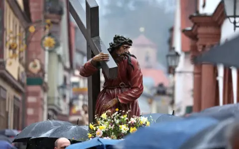 Prozession am Karfreitag: Jesus trägt das Kreuz. Gläubige mit Regenschirmen gedenken.