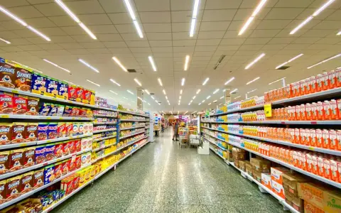 Alejka w supermarketach, pełna produktów na półkach. Widać kartony z płatkami śniadaniowymi i napojami. To typowe sklepy po angielsku, gdzie można znaleźć wszystko.