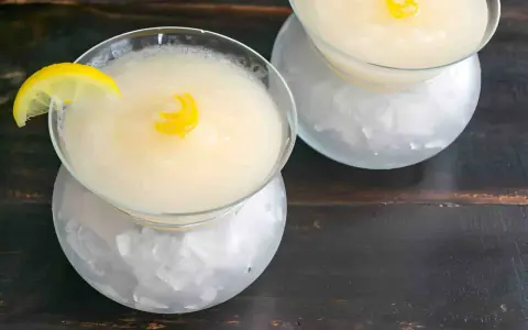Dos copas de sorbete de limón, una con rodaja de limón y rizo de cáscara, servidas sobre hielo picado.