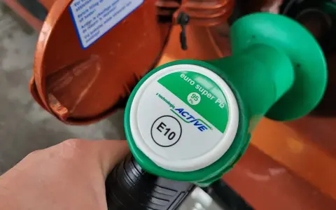 Dłoń trzyma zielony pistolet dystrybutora z napisem "euro super Pb 95 ACTIVE E10". To benzyna e10.
