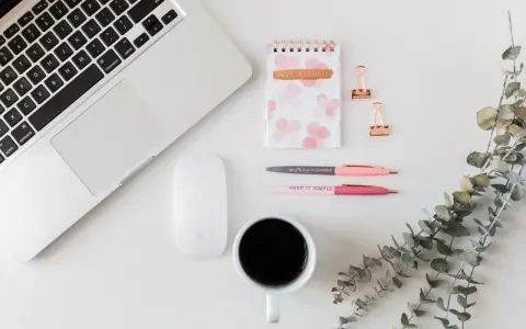 Ein Schreibtisch mit Laptop, Maus, Notizbuch, Stiften und Kaffee. Ideal für Lehrer, die ihr Zeitmanagement verbessern wollen.