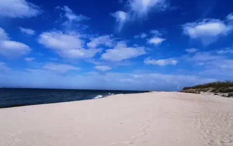 Pusta plaża z wydmami i latarnią morską, idealna na weekendowe odkrywanie magicznych miejsc nad Bałtykiem.