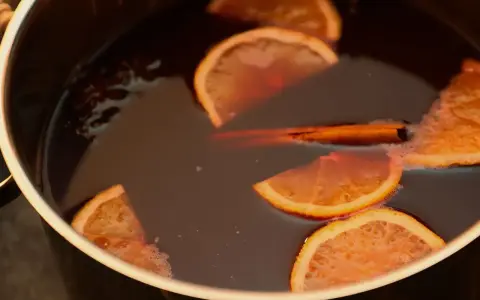 Une marmite remplie d'un liquide sombre, avec des tranches d'orange, un bâton de cannelle et de l'anis étoilé. Parfait pour une recette punch simple et réconfortante.