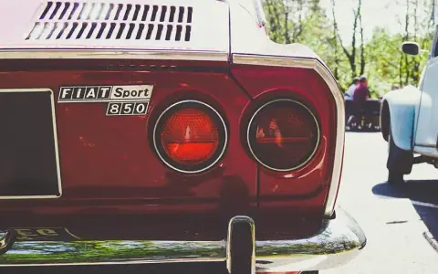 Dettaglio posteriore di una Fiat Sport 850 rossa, con i suoi iconici fanali rotondi. Un pezzo di storia automobilistica, un vero art 102 cds.